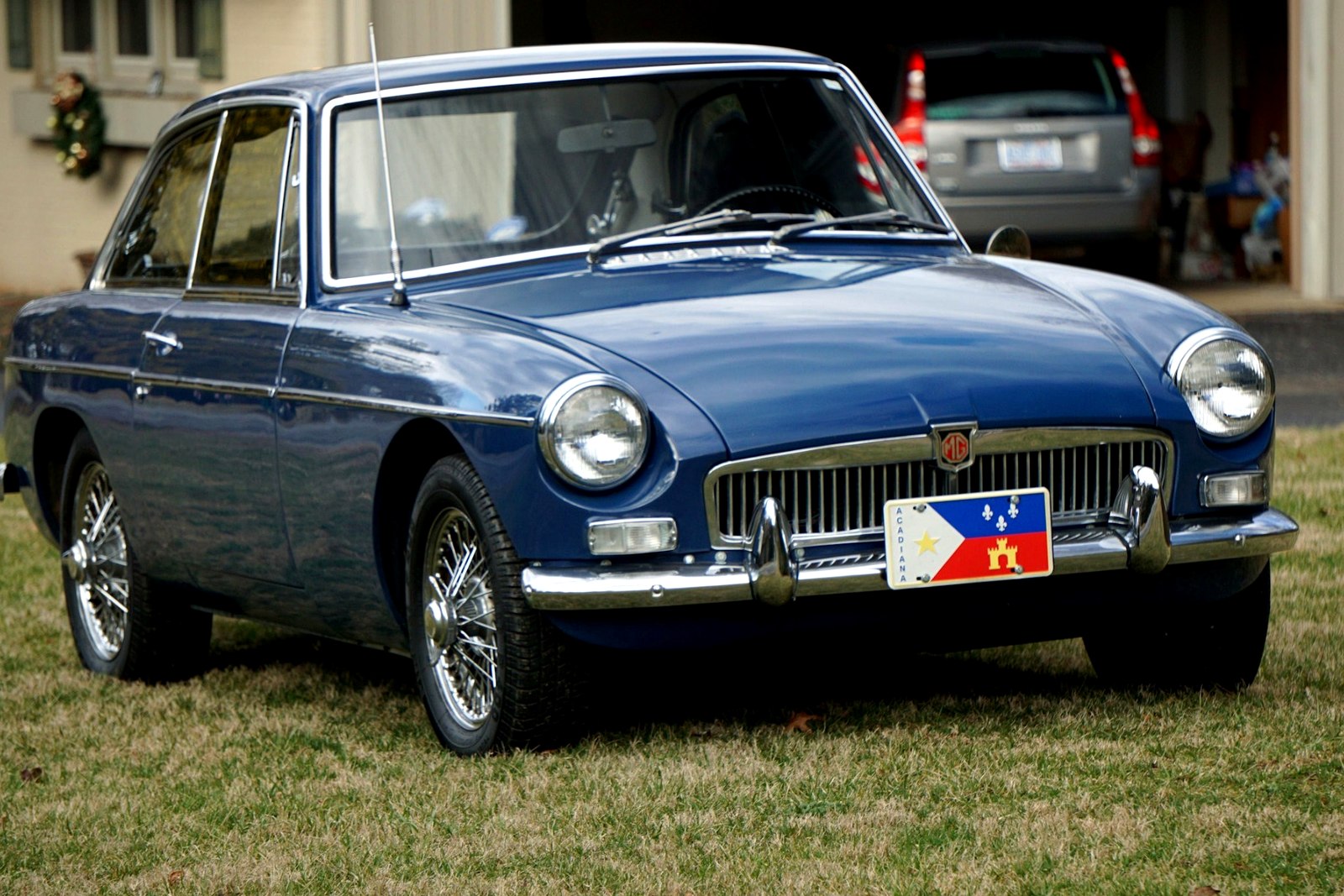 Classic blue MG coupe photographed from the front three-quarter angle on a residential lawn.